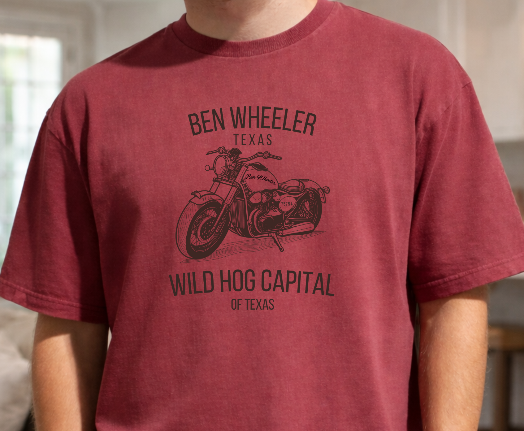 red short-sleeve t-shirt with black graphic of a vintage motorcycle and the words Ben Wheeler Texas and Wild Hog Capital of Texas, worn by a person with hands in their pockets.