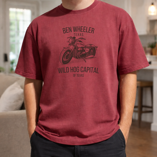 red short-sleeve t-shirt with black graphic of a vintage motorcycle and the words Ben Wheeler Texas and Wild Hog Capital of Texas, worn by a person with hands in their pockets.