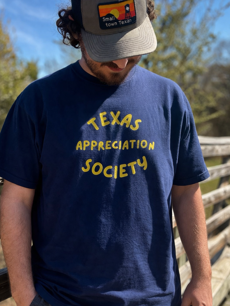 person wearing navy Texas Appreciation Society t-shirt outdoors on a wooden bridge in Texas