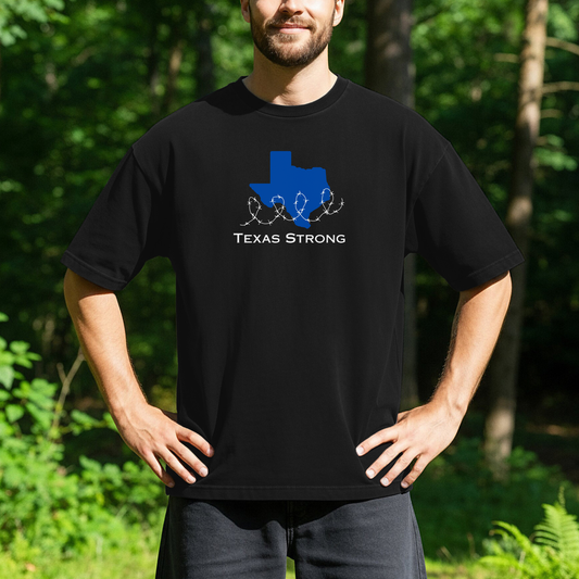 person standing outdoors wearing a black t-shirt with a blue outline of the state of Texas wrapped in barbed wire and the text, Texas Strong.